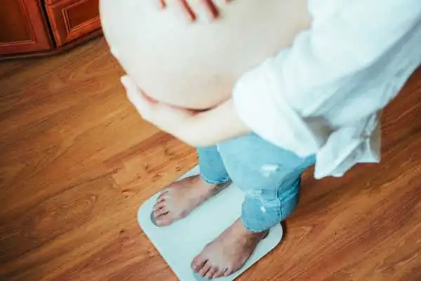 Image of woman weighing herself and experiencing weight gain through pregnancy Market Drayton